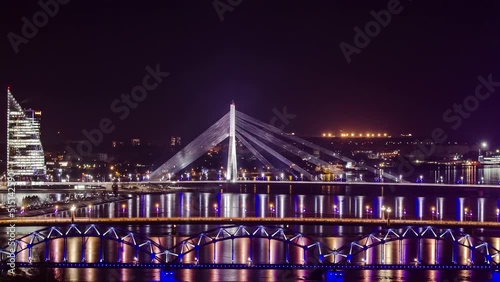 Scenic Night View Of Illuminated Vansu Bridge And Swedbank Headquarters Building In Riga, Latvia. Railway Bridge (Dzelzceļa Tilts) In Foreground. timelapse photo