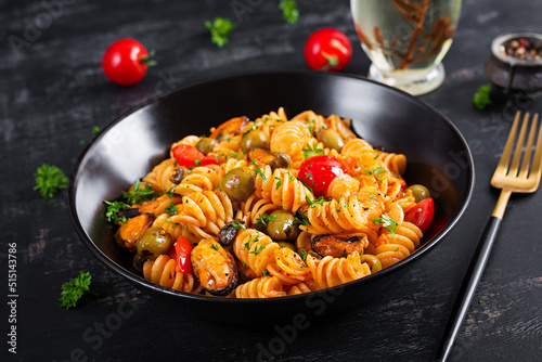 Classic italian pasta fusilli marinara with mussels, green olives and capers on dark table. Fusilli pasta with sauce marinara