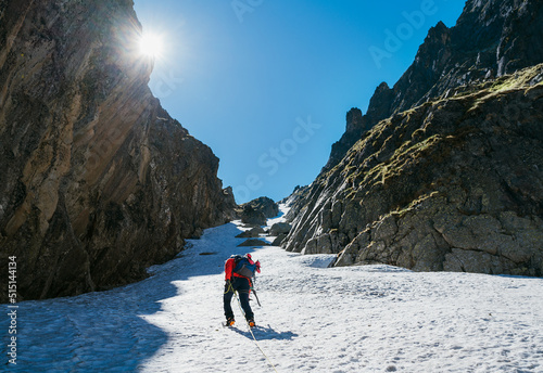 Team roping up woman with climbing axe dressed high altitude mountaineering clothes with backpack walking by snowy slope in the couloir with backlight sun on blue sky. photo