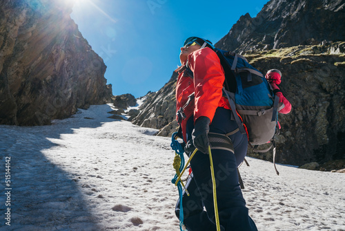 Tela Team roping up woman dressed high altitude mountaineering clothes and harness climbing with backpack by snowy slope in the couloir with backlight sun on blue sky