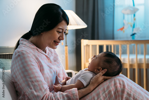 Cuadro en lienzo portrait smiling asian new mom in pajamas is looking at her cute yawning baby who’s sitting on her laps in the bedroom at bedtime