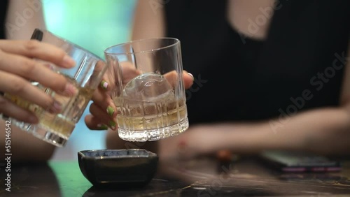 closeup shot of Asian female hands holding whisky glasses chatting at a bar