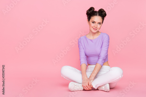 Portrait of attractive calm cheerful brunette girl sitting on floor isolated over pink pastel color background