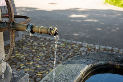 Old vintage stone and forged steel public drinking water fountain in a small village in Switzerland, Europe. Clear pouring water from the faucet, close up shot, no people