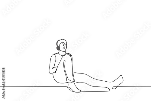 man in overhead headphones sits leaning against the wall - one line drawing vector. concept listening to music alone