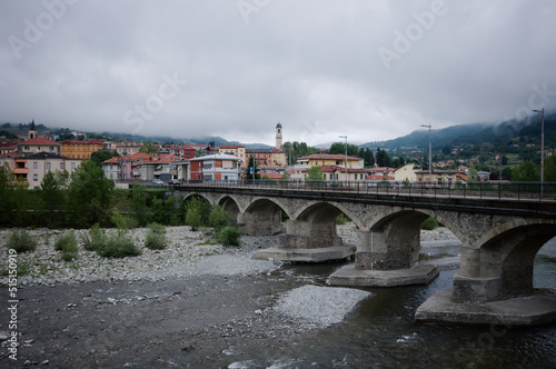 Borgo Val di Taro, Italy - May, 2022: Panoramic view of Borgotaro town in rainy day. Bridge across Taro river, townscape of Italian village and overcast sky in Appenins, Parma province, Emilia-Romagna