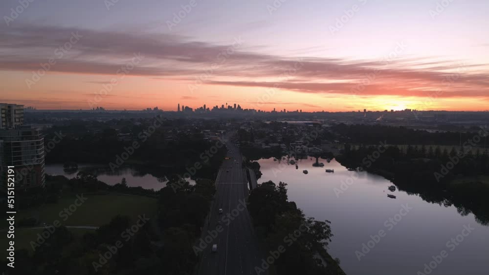 Cinematic aerial landscape shot rises from a highway to reveal a Sydney city skyline at the horizon during a beautiful sunrise in the morning Cinematic aerial landscape shot rises from a highway to reveal a Sydney city skyline at the horizon during a beautiful sunrise in the morning