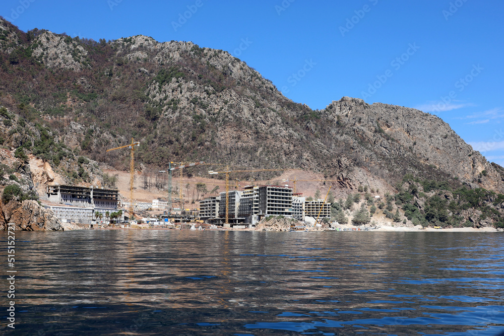 Construction of hotel buildings on a mountain beach in Mediterranean sea. Development of summer resort in Turkey