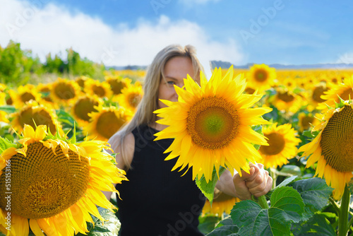 Beautiful blonde woman in black dress enjoying nature . Happy smiling female standing in sunflowers field.