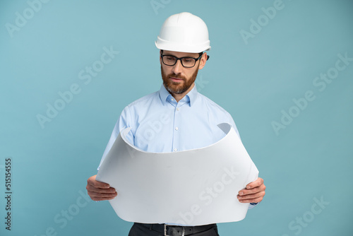 Architect man with concentrated face in builder safety helmet looking at the blueprints over isolated background. Engineer concept
