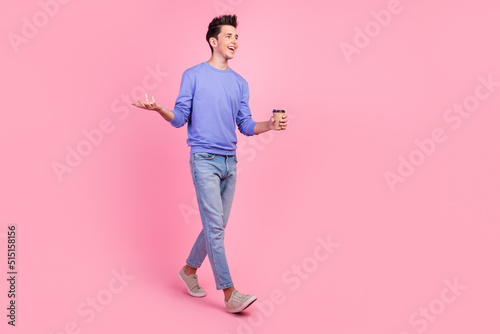 Full length of young caucasian happy smiling man hold paper cup of hot coffee drink go isolated on pastel color background