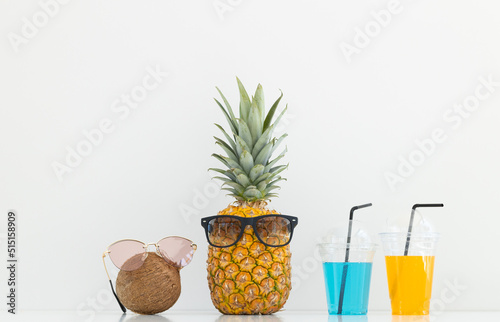 incised pineapple and coconut with sunglasses near a glass of juice and a cocktail straw