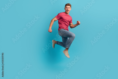 Full body profile side photo of young excited man run jump hurry activity isolated over blue color background