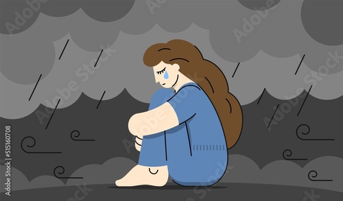 A sad woman crying sadly with her hands wrapped around her knees in the rain on a gray windy day under storm clouds.