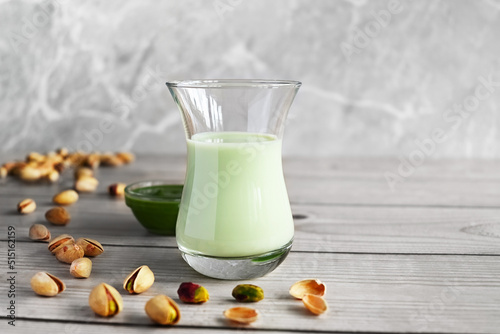 Pistachio milk in the glass and pistachio paste  on the wooden background
