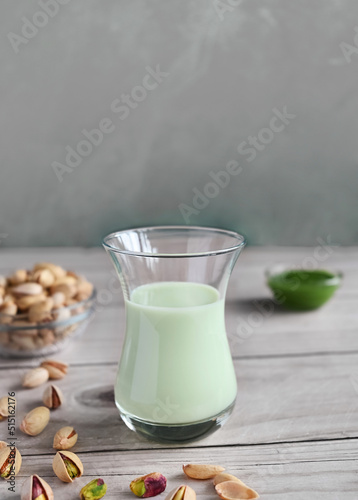 Pistachio milk in the glass and pistachio paste  on the wooden background