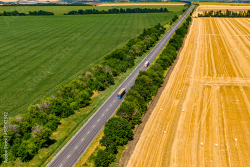 cargo delivery. trucks driving on asphalt road along the green fields whith rolls of haystacks. photo