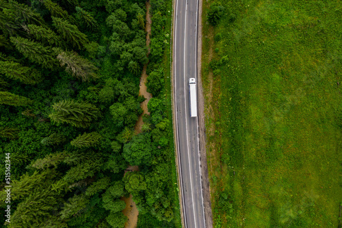 white truck driving on asphalt road on the highway. road through beautiful green forest. seen from the air. Aerial top view landscape. drone photography. cargo delivery photo