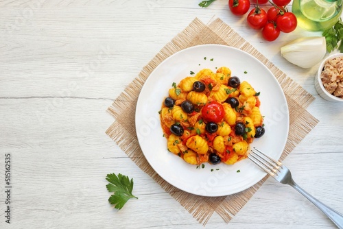 Italian Traditional Dish"Gnocchi con tonno,pomodorini e olive",gnocchi with canned tuna in olive oil,cherry tomatoes,olives,onions,olive oil,parsley and peppers on plate with white wood background