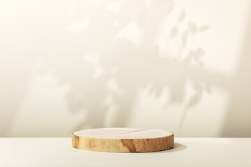 Wood slice podium with leaves  and window shadows on beige background for cosmetic product mockup