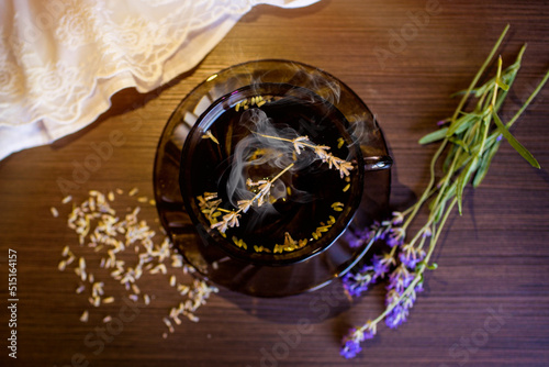 Herbal tea from lavender in a vintage cup on a dark wooden table. Near sprigs of fresh lavender and dried flowers. Steam comes out of the cup. Top view. 