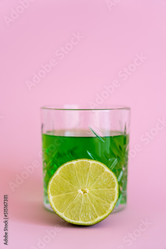 green fresh lime near alcohol drink in glass on pink.