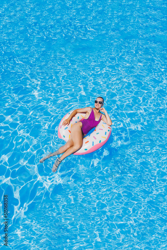 Beautiful slim young woman in a swimsuit enjoying the water park floating in an inflatable big ring on a sparkling blue pool smiling at the camera. Summer vacation.