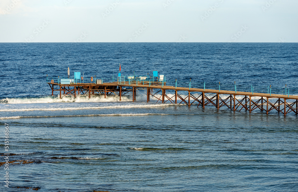 Seascape of the Red Sea near Marsa Alam, Egypt, Africa. Wooden pier above the coral reef used for diving, snorkeling and swimming with the red flag. Waves breaking on the coral reef.