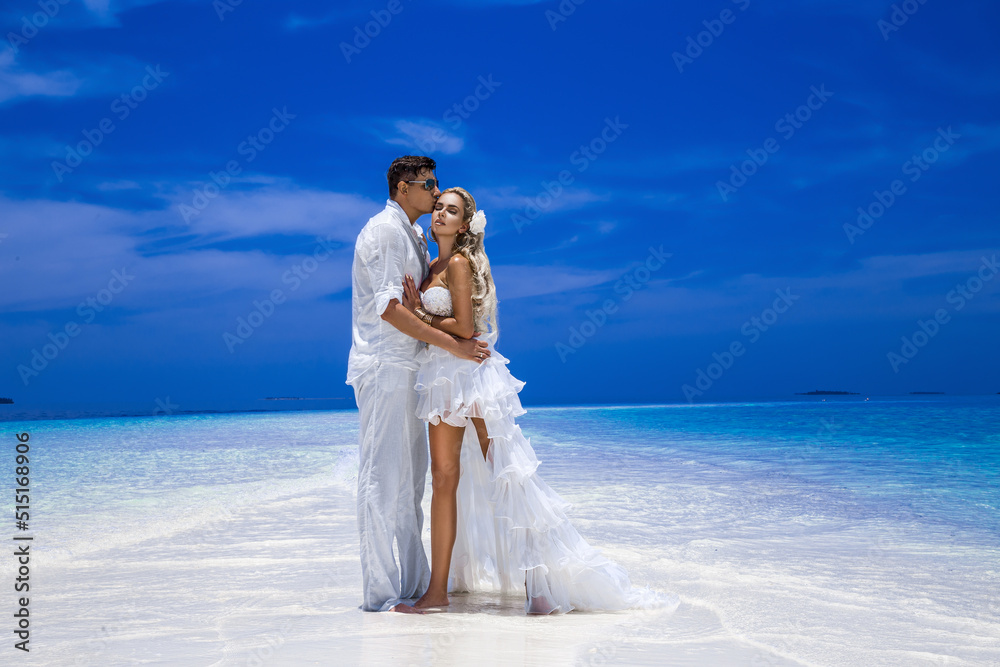 Summer love. Beautiful happy young couple in wedding clothes is standing on a beach in the Maldives. Engagements and wedding on the beach on the paradise island of Maldives. Luxury travel. Summer love. Beautiful happy young couple in wedding clothes is standing on a beach in the Maldives. Engagements and wedding on the beach on the paradise island of Maldives. Luxury travel.