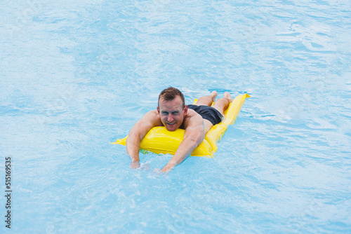 Handsome man in swimming shorts with an inflatable yellow mattress in the pool. Summer vacation in the hotel