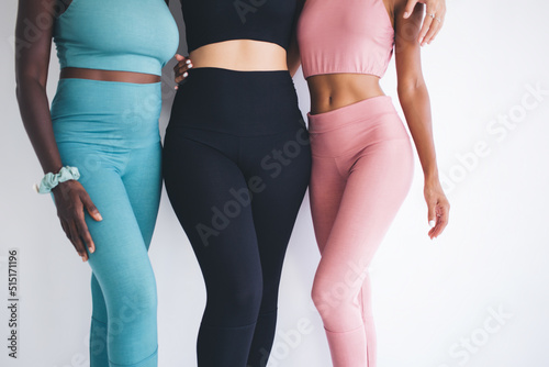 Fototapeta Naklejka Na Ścianę i Meble -  Cropped diverse female in trendy tracksuits posing during sportive photo session in gym aerobic studio, unrecognizable multicultural yoga partners enjoying collaborative workout teamwork indoors