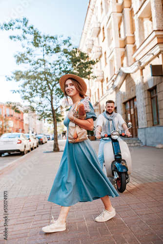 young couple riding a vintage scooter in the street in sunny summer day