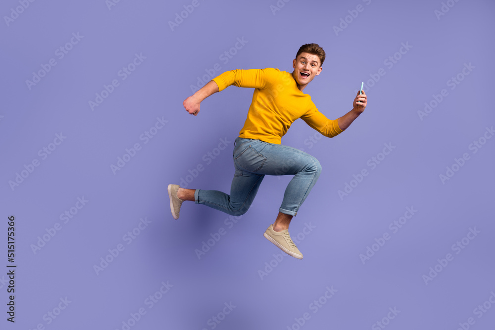 Full body profile side photo of young guy jumper runnner use mobile share isolated over violet color background Full body profile side photo of young guy jumper runnner use mobile share isolated over violet color background