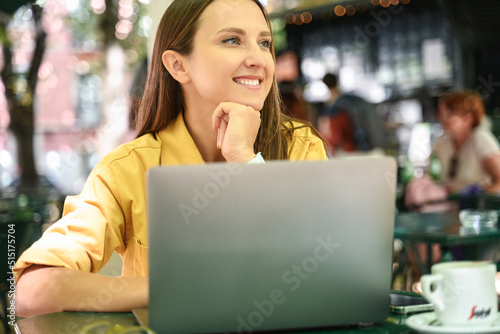 Attractive inspired female freelancer enjoying remote work sitting at the table in summer cafe outdoors, smiling woman using laptop computer sitting in the park
