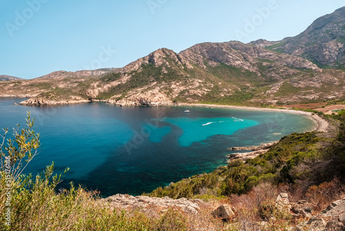 Several jet skis and a catamaran in a large rocky cove on the west coast of Corsica and turquoise Mediterranean sea