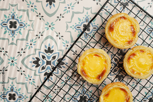 Traditional portuguese vanilla pudding puff pastry pastel de nata on black oven rack on blue tiles background - top view photo