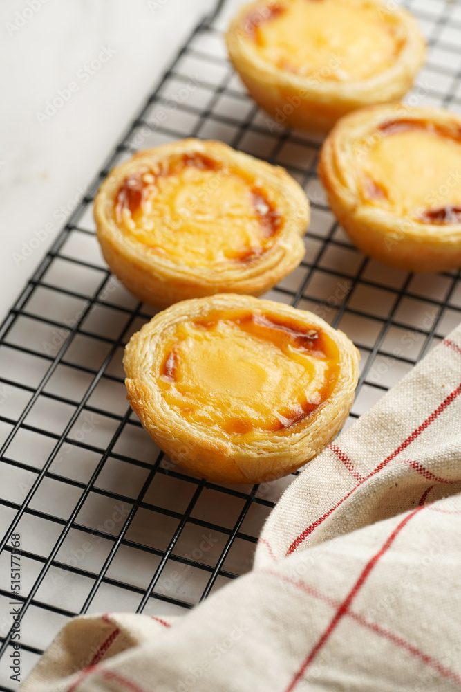 Traditional portuguese vanilla pudding puff pastry pastel de nata on black oven rack on marble background with checkered kitchen towel Traditional portuguese vanilla pudding puff pastry pastel de nata on black oven rack on marble background with checkered kitchen towel