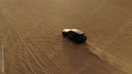 Aerial tracking shot of a SUV black car driving in the Arabian desert Dubai UAE at sunset