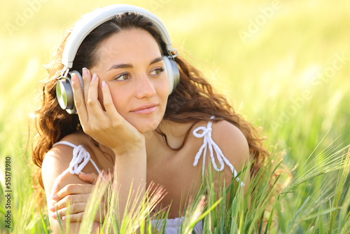 Woman listening to music looking at side in a wheat field © Antonioguillem