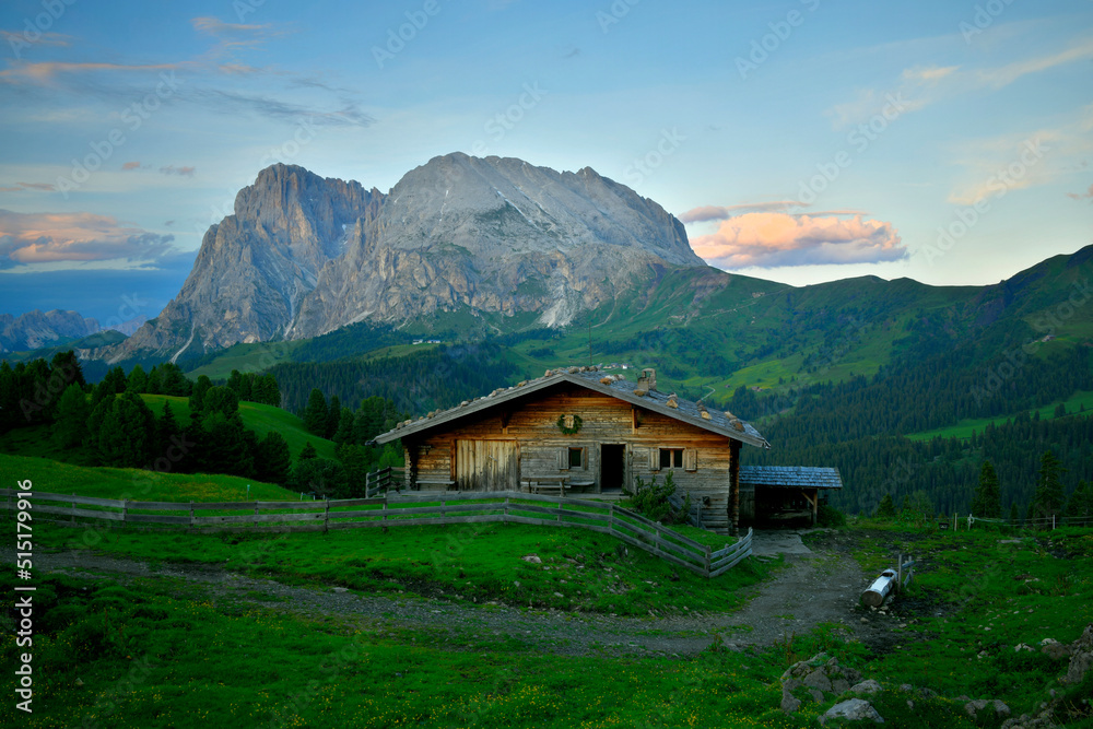 Eine Urige und Alte Berghütte aus Holz auf der Seiser Alm und im Hintergrund sieht man den Mächtigen Lang- und Plattkofel in der Dämmerung.