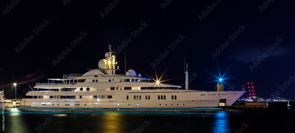 Obraz premium Yacht illuminated by night lights of a port
