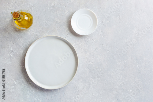 White empty serving dish, small plate and olive oil pitcher, top view