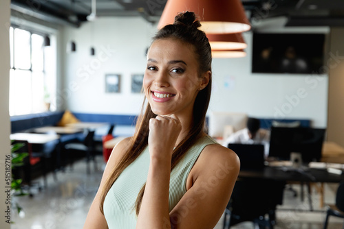 Portrait of smiling young caucasian businesswoman with hand on chin in creative office