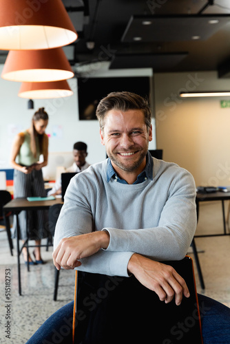 Portrait of smiling caucasian mid adult businessman sitting on chair in creative office © wavebreak3