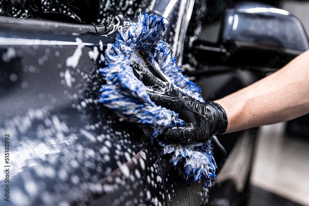 car wash employee thoroughly washes a modern car with a dedicated washing mitt