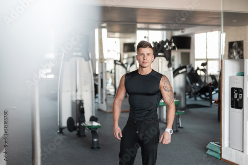 Sports handsome bodybuilder trainer guy with a muscular healthy body with a tattoo in a black t-shirt mock up with sportswear in the gym photo