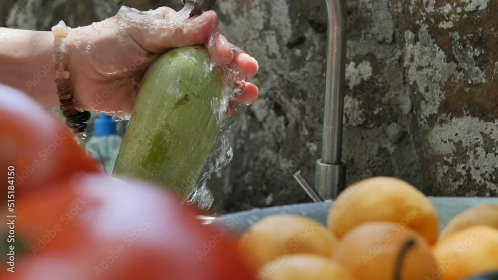 a woman washes zucchini with her hands under a stream of clean water