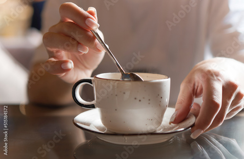 Closeup of female hands with french manicure holding cozy ceramic white mug of tea or coffee. Relax and comfort at home, cafe. Drinking hot cocoa. Empty space for text on blurry background, backplate