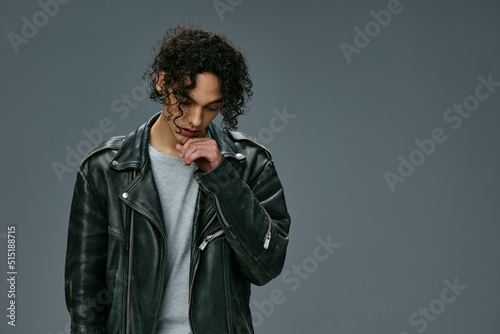 Handsome fashionable stylish tanned curly man leather jacket posing isolated on over gray studio background. Cool fashion offer. Huge Seasonal Sale New Collection concept. Copy space for ad