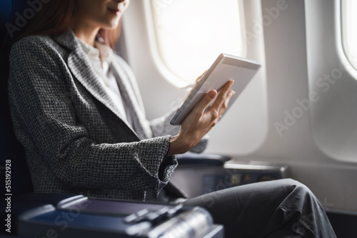 A successful asian businesswoman or female entrepreneur in formal suit in a plane sits in a business class's seat and uses a tablet computer during flight